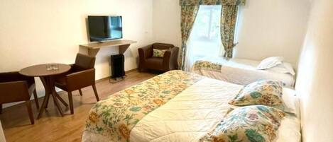 A hotel room with a bed, a desk, a chair, a TV, and a window with curtains.