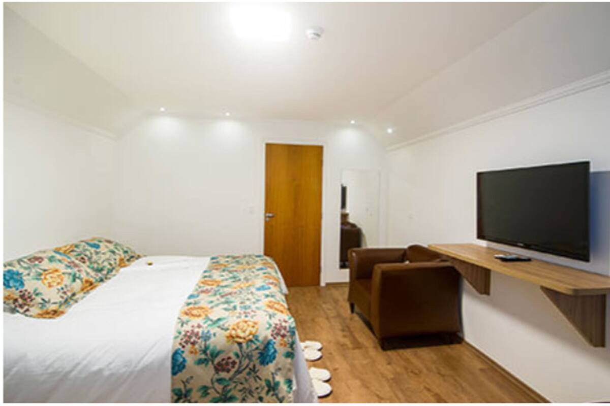 A modern hotel room with a bed, a TV, a desk, and a chair.
