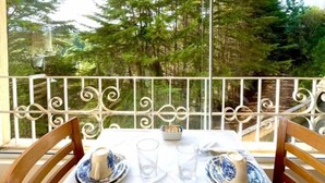 A balcony with a table set for two, overlooking a forested area. - Pousada Itália Moderna (Campos do Jordão)