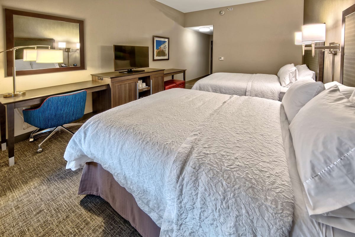 Une chambre d’hôtel avec deux lits, un bureau avec un ordinateur, une chaise et un téléviseur.