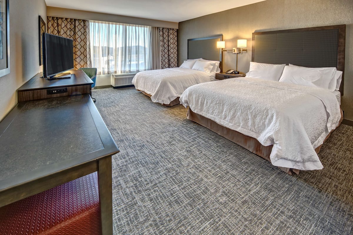 Une chambre d’hôtel avec deux lits, un bureau avec une télévision, une fenêtre avec des rideaux et un mur décoré d’un motif.