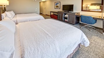 A hotel room with two beds, a desk, a chair, a television, and a mirror.
