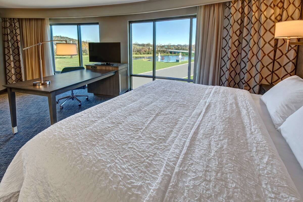 Une chambre d’hôtel dotée d’un grand lit, d’un bureau avec une chaise, d’une télévision et offrant une vue sur un terrain de golf grâce à de grandes fenêtres.