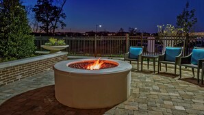 A circular outdoor fire pit with a brick wall and seating area with chairs and a table. - Hampton Inn & Suites Franklin Berry Farms (Franklin)