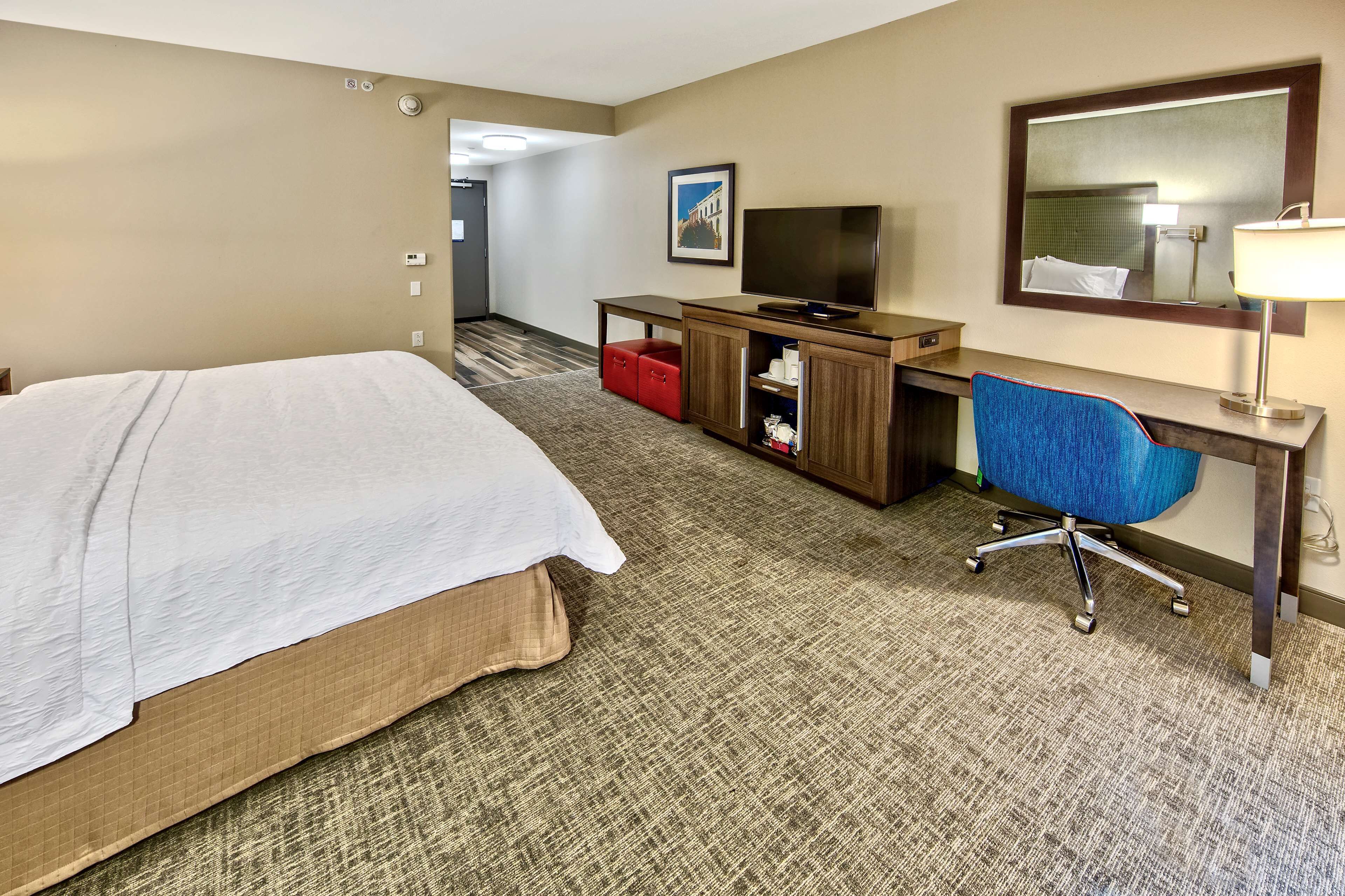 A hotel room with a bed, a desk with a computer, a TV, and a mirror.