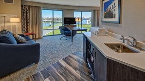 A hotel room with a large window, a sofa, a desk, a TV, and a kitchen area. - Hampton Inn & Suites Franklin Berry Farms (Franklin)