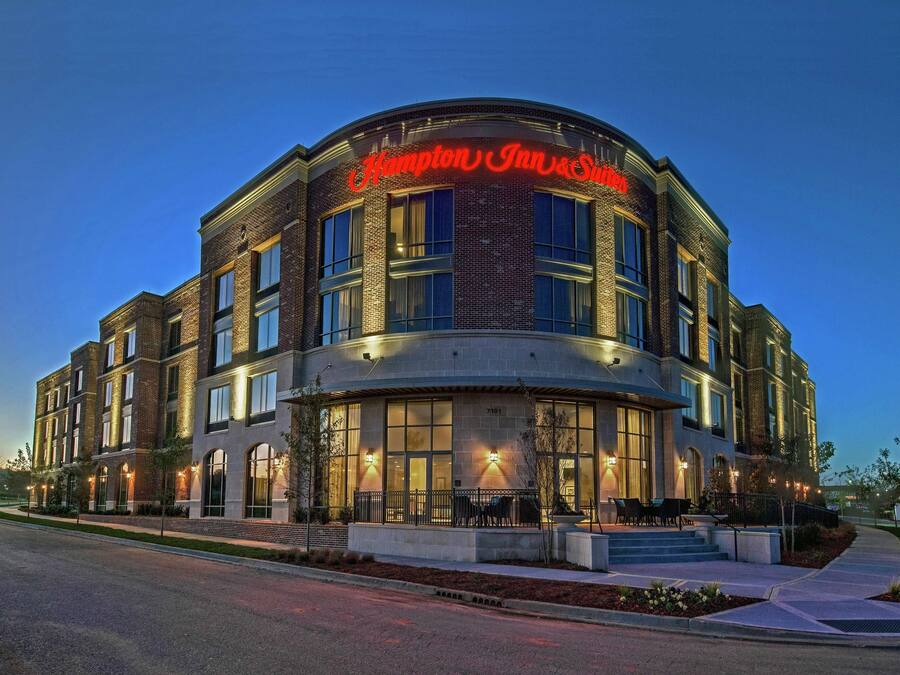 Et Hampton Inn & Suites hotel med murstensfacade, store vinduer og en godt oplyst indgang.