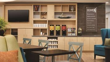 Quarto de hotel moderno com TV de tela plana na parede, um espaço para café com opções descafeinadas e gourmet, e um aviso sobre garantia de conforto.