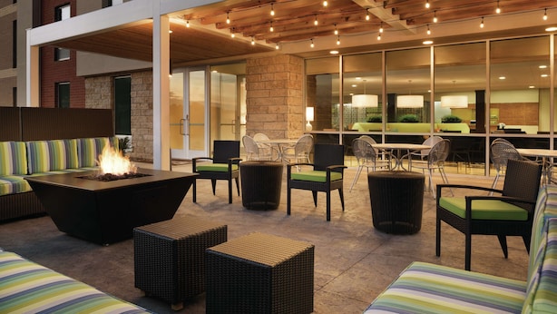 Un área de estar al aire libre con una chimenea, muebles de mimbre y vista al interior.