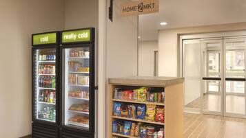 Een hotel lobby met twee gekoelde drankautomaten, waarvan een gelabeld is met 'koud' en de andere met 'echt koud', en een vitrine met snacks.