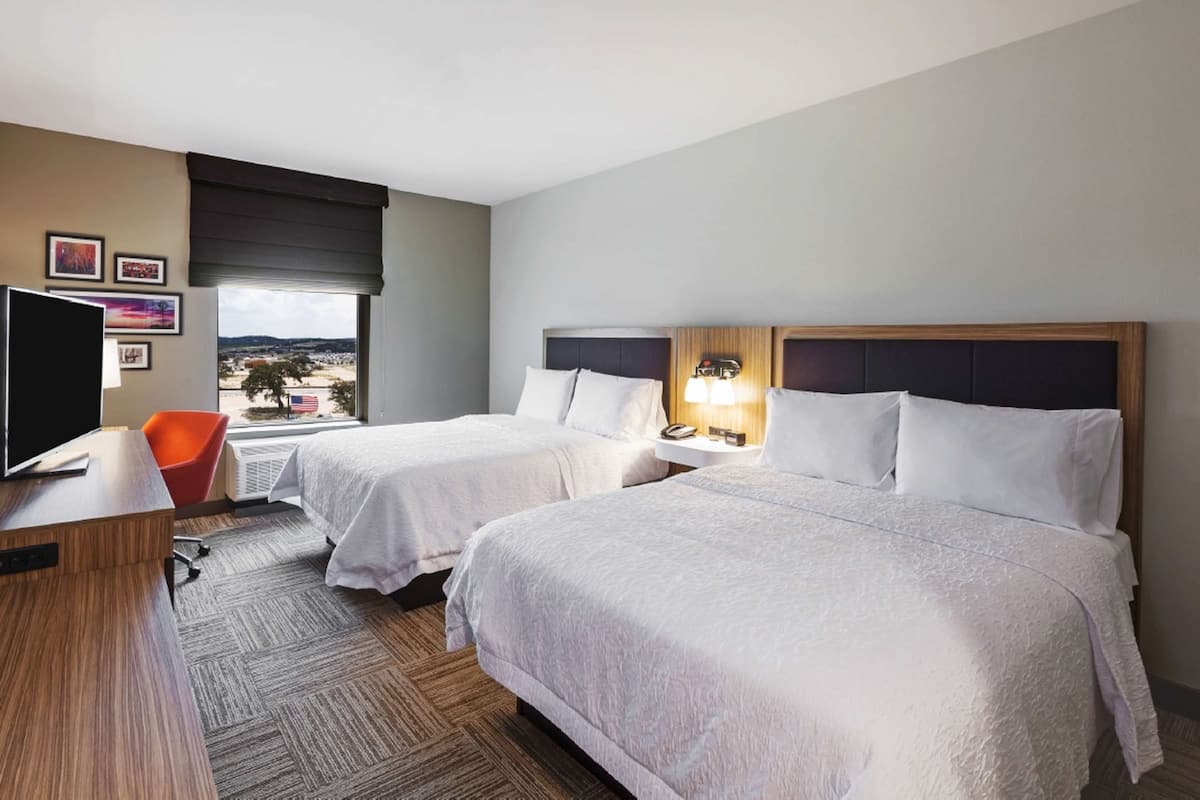 A hotel room with two beds, a desk with a TV, a chair, and a window with a view.