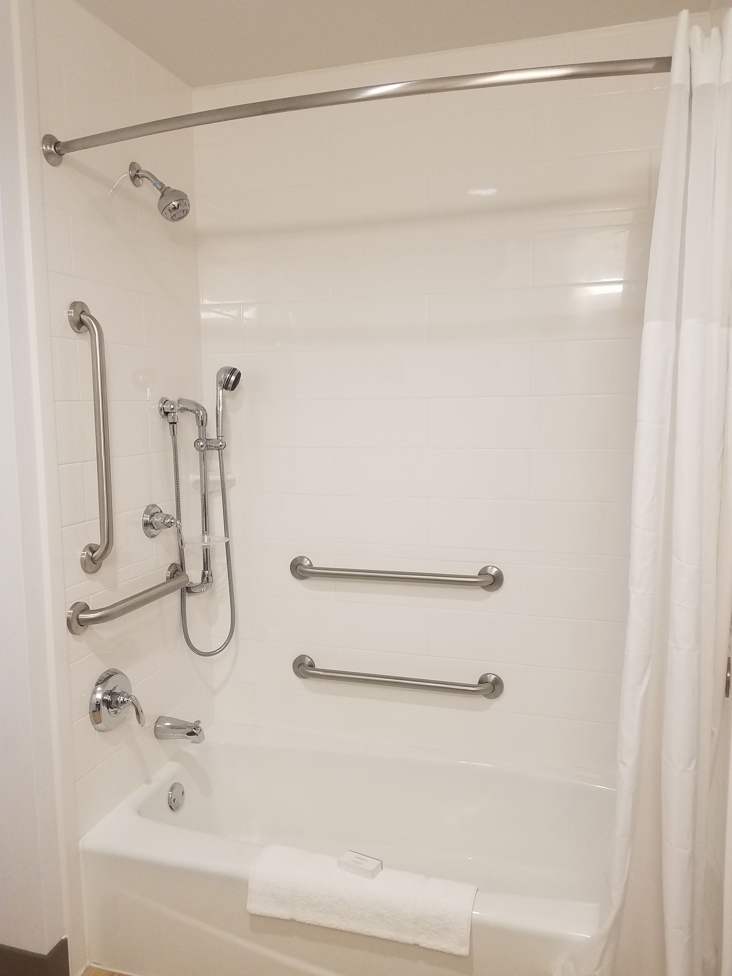 Un baño moderno con cabina de ducha, barras de apoyo y bañera.