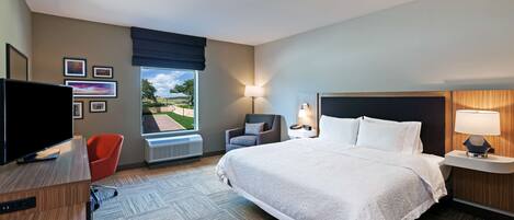 Une chambre d’hôtel avec un grand lit, un bureau avec une télévision, une chaise, une lampe et une fenêtre donnant sur l’extérieur.