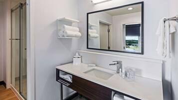 Un baño moderno con ducha de vidrio, tocador blanco y un espejo grande.