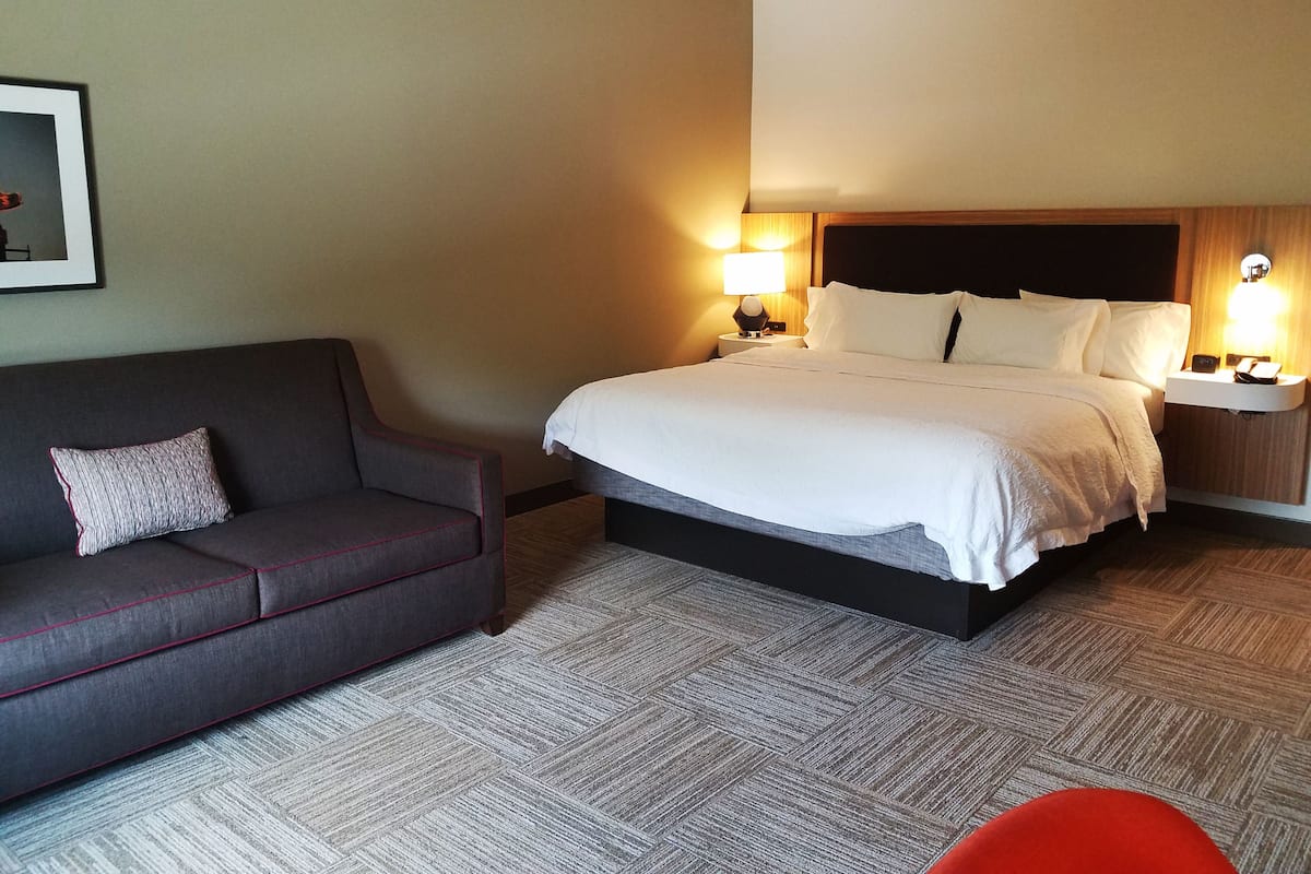 A hotel room with a bed, a sofa, two bedside tables with lamps, and a framed picture on the wall.