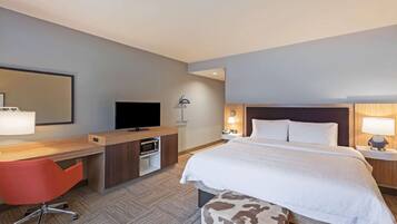 Ein Hotelzimmer mit einem Bett, einem Schreibtisch mit Fernseher, einem roten Sessel und einem Nachttisch mit Lampe.