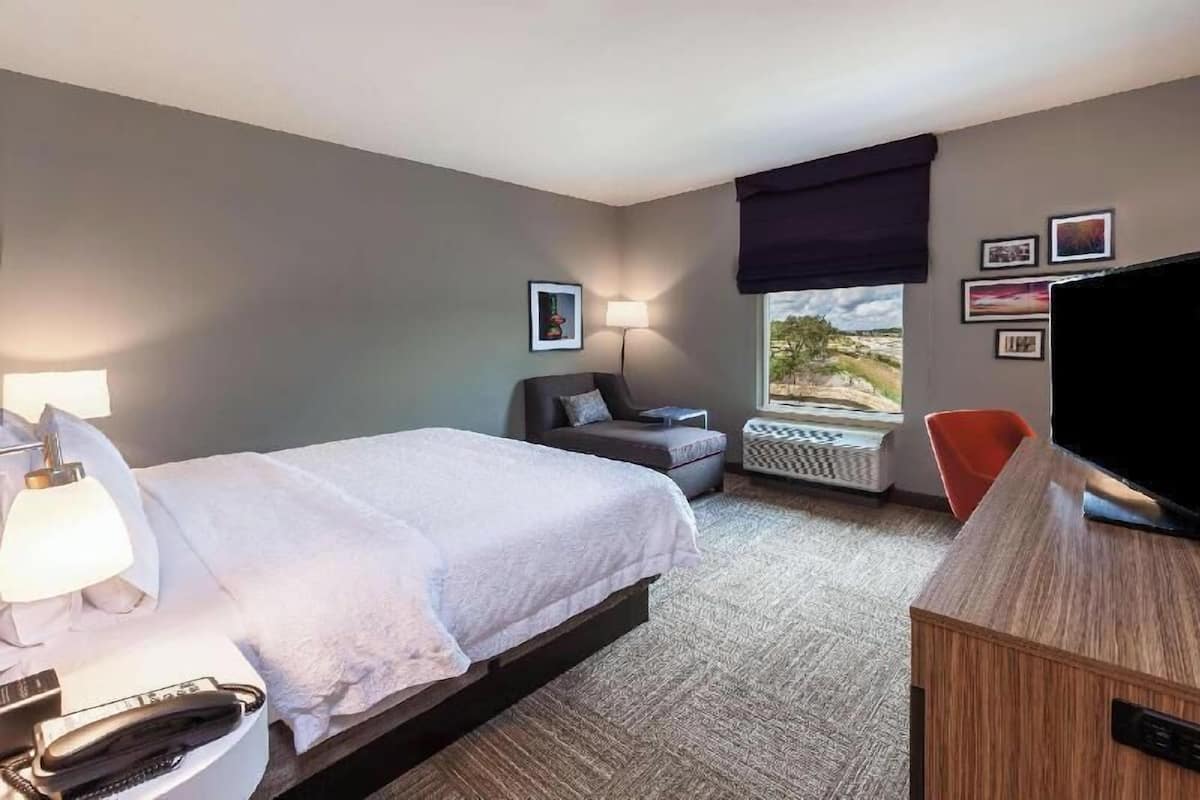 A hotel room with a bed, a desk, a chair, a TV, a lamp, and a window with a view.
