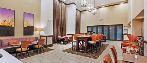 A hotel lobby with a reception desk, seating areas, and a dining space.