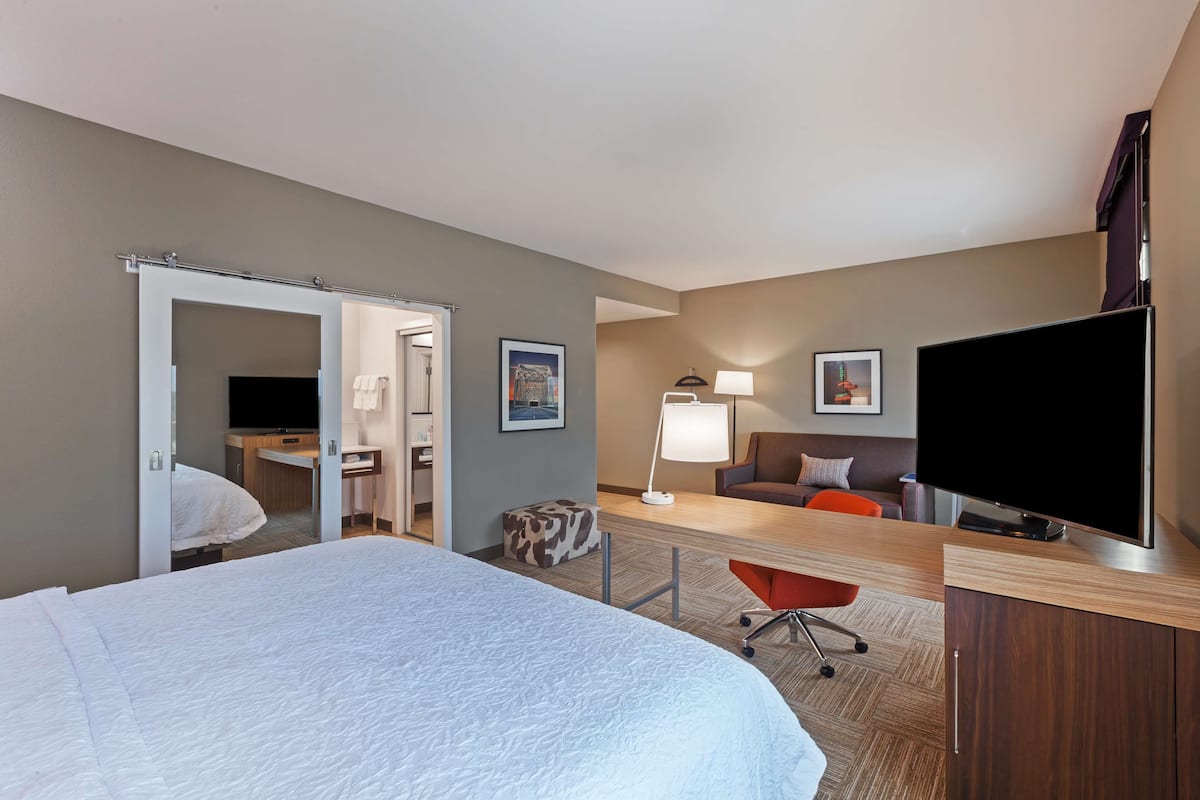 A hotel room with a large bed, a desk with a computer, a TV, and a chair.