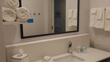 A modern bathroom with a large mirror, white sink, towel rack, and a tissue dispenser.