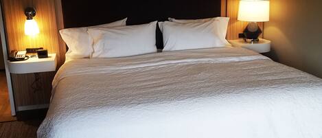 Een hotelkamer met een groot bed, twee nachtkastjes, een lamp en een gestreept voetenbankje.