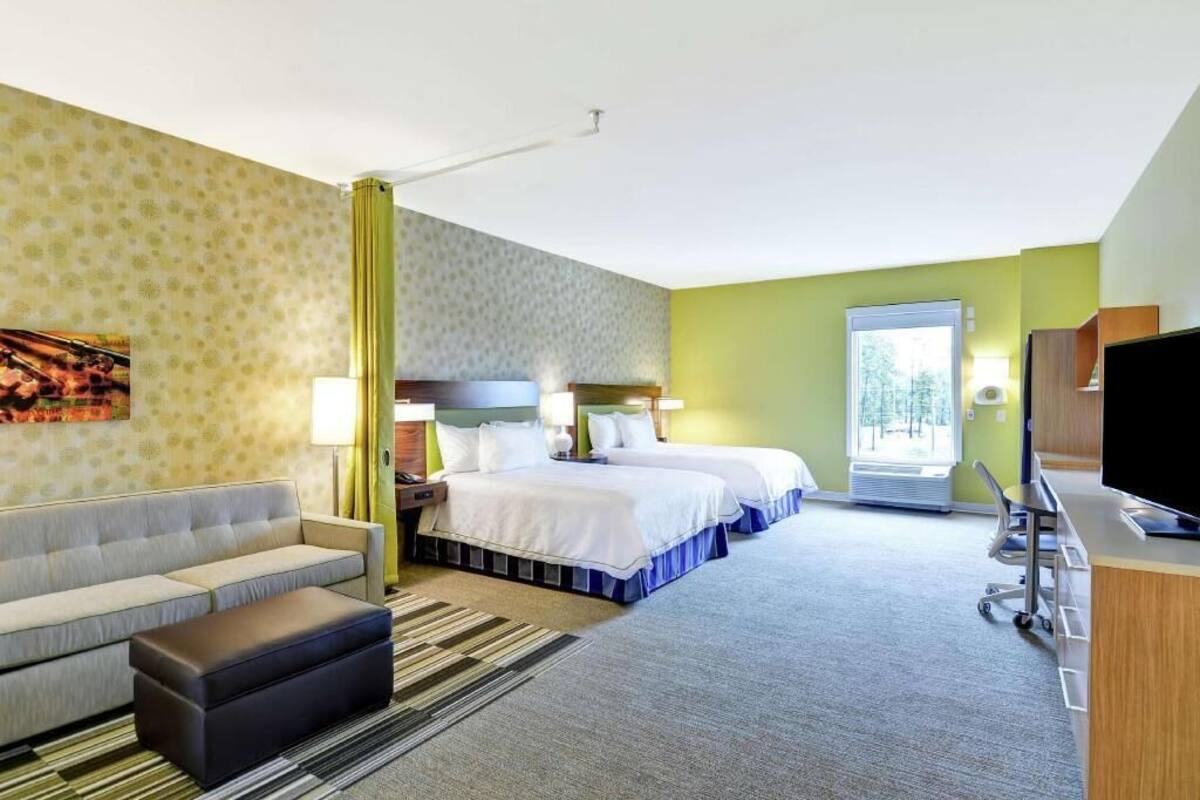 A hotel room with two beds, a sofa, a desk with a TV, and a window.