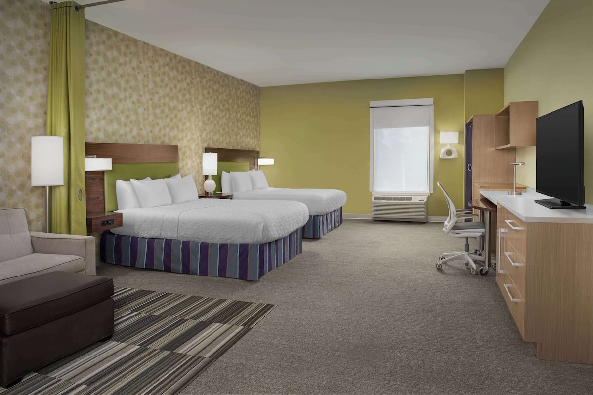 A hotel room with two beds, a desk, a TV, and a chair.