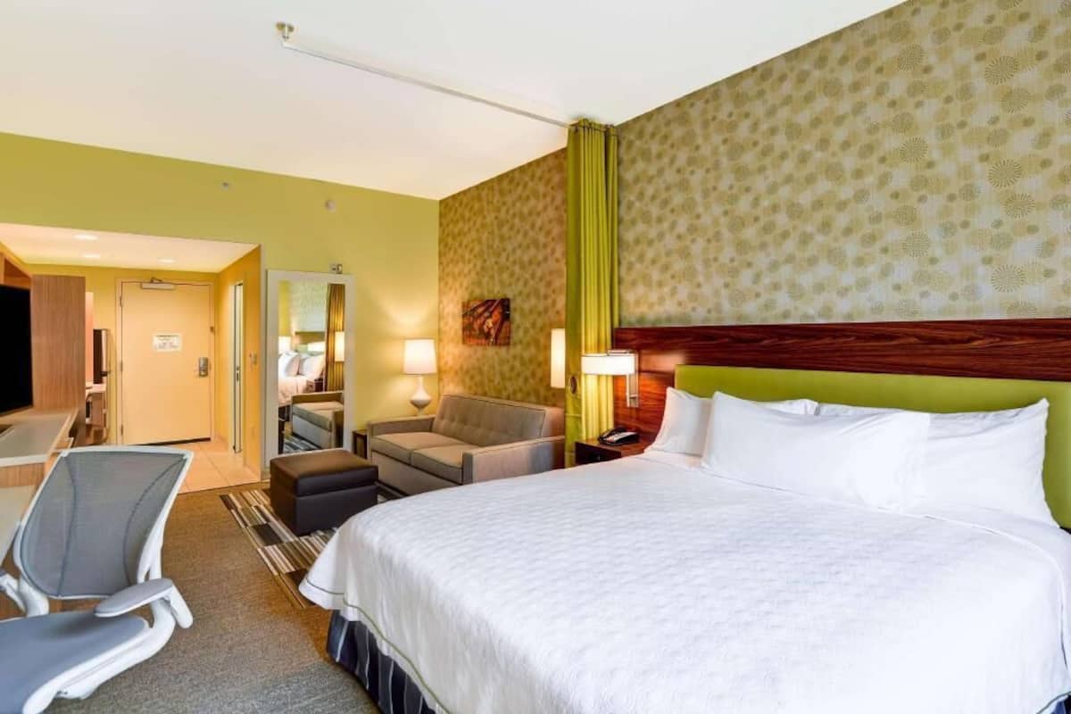 Una habitación de hotel con una cama, un escritorio, una silla, un sofá y un espejo.