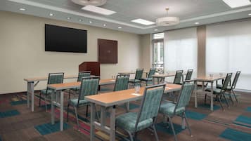 Une salle de conférence équipée de plusieurs tables et chaises, d’un grand téléviseur à écran plat et d’une fenêtre avec des stores.