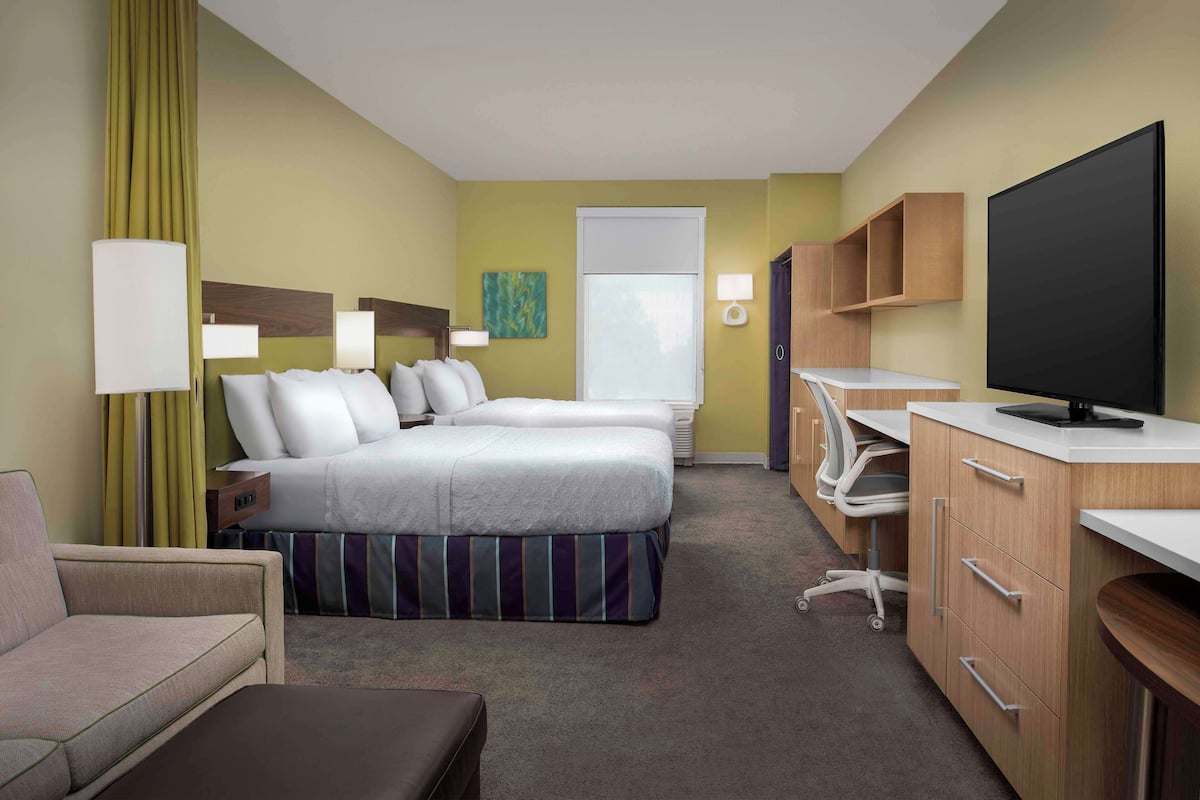 A hotel room with a bed, two bedside tables, a desk with a chair, a television, and a window.