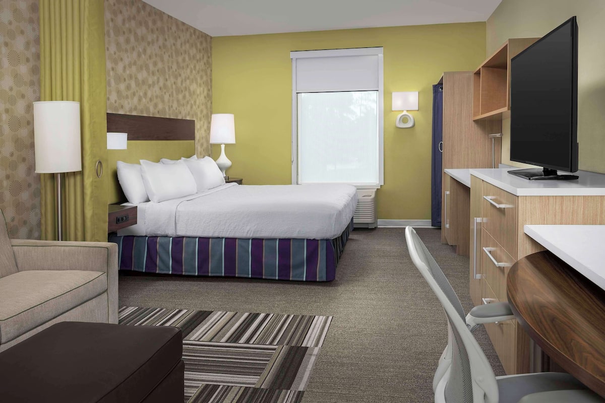 A hotel room with a bed, a desk, a television, and a window with blinds.