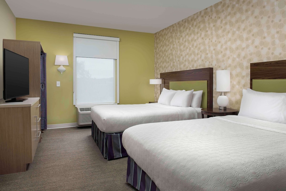 A hotel room with two beds, a TV, and a window.