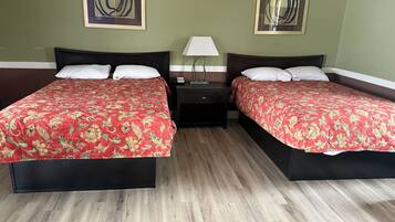 Ein Hotelzimmer mit zwei Betten, jeweils mit einer roten, floralen Tagesdecke, einem Nachttisch mit Lampe und zwei abstrakten Bildern an den Wänden.