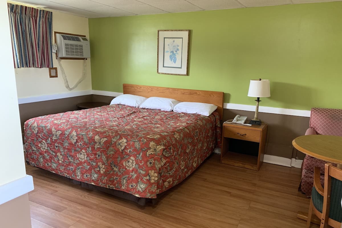 Une chambre d’hôtel avec un grand lit, une table de chevet avec une lampe, une chaise et un tableau encadré au mur.