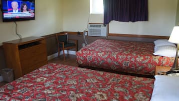 A hotel room with two beds, a desk, a chair, a TV, and an air conditioning unit.