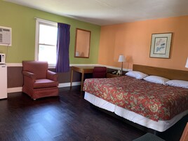 Una habitación de hotel con cama, escritorio, silla, espejo y ventana con cortinas.