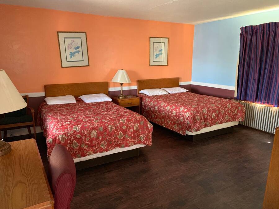 A hotel room with two beds, a nightstand, a lamp, and framed pictures on the wall.