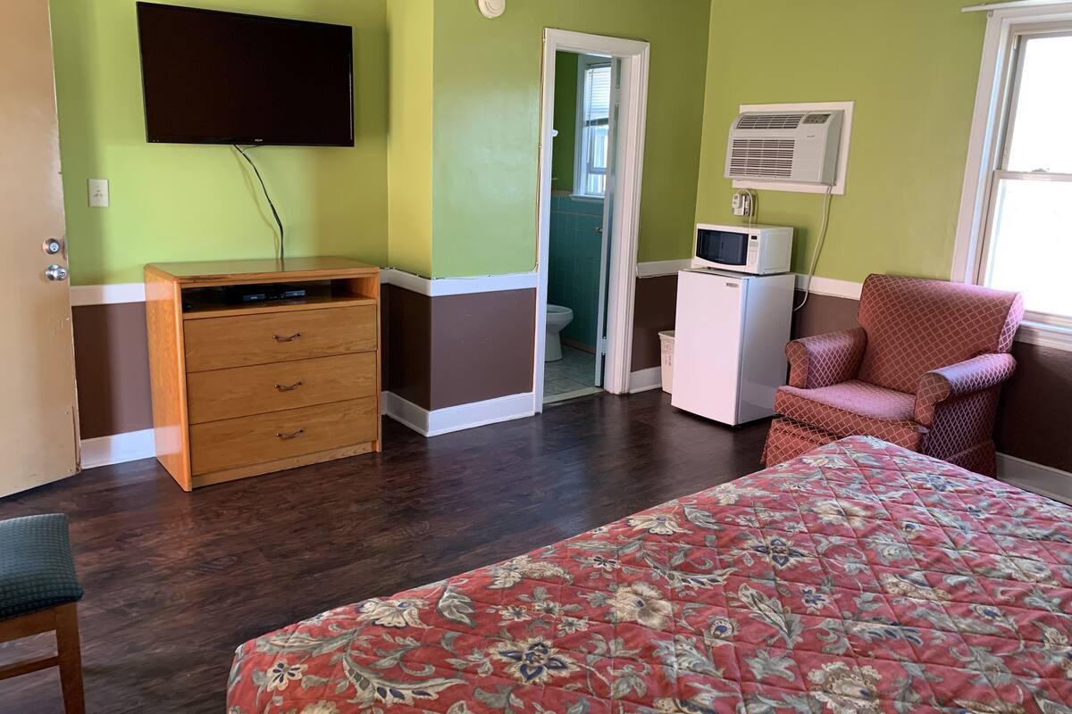 Une chambre comprenant un lit, une commode, un téléviseur, un four à micro-ondes, un climatiseur et une chaise.
