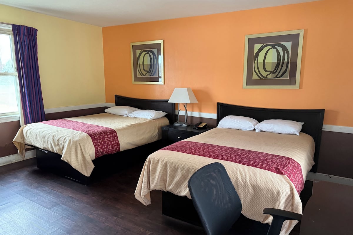 Une chambre d’hôtel avec deux lits, une table de chevet avec une lampe, une chaise et des œuvres d’art accrochées aux murs.