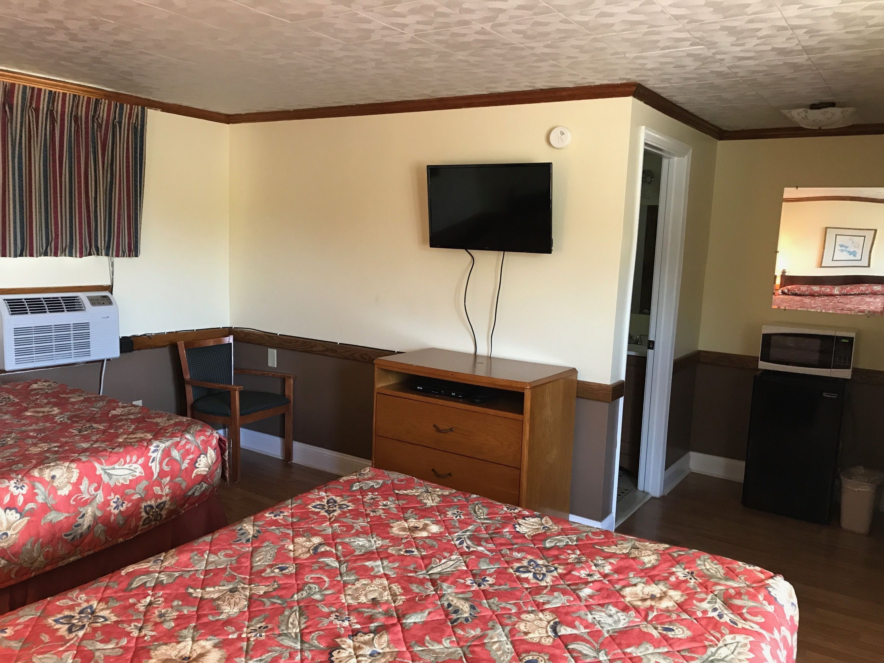 Ett hotellrum med två sängar, ett skrivbord med en stol, en tv, en luftkonditioneringsanläggning och en mikrovågsugn.