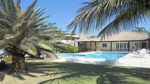 A residential property with a swimming pool, palm trees, and a house with a tiled roof. - Casa na Beira da Praia de Geribá (Búzios)