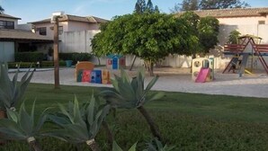 A playground with colorful play structures and a tree in the background. - Casa na Beira da Praia de Geribá (Búzios)