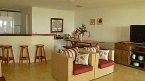A living room with a sofa, wooden stools, a dining table, and a TV. - Casa na Beira da Praia de Geribá (Búzios)