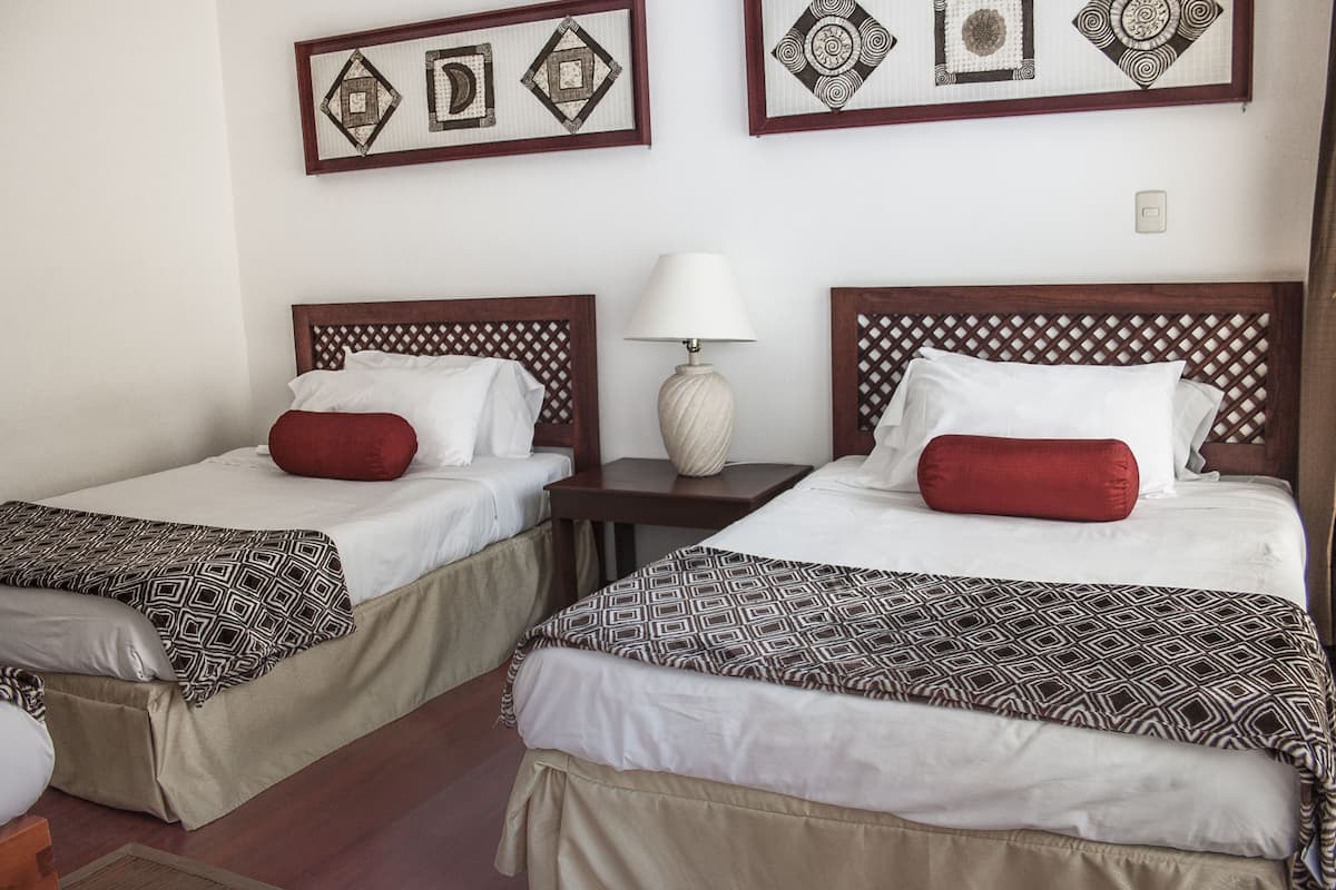 Dos camas individuales con ropa de cama estampada, una mesita de noche con lámpara y decoración en la pared.