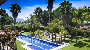 Une piscine entourée d’un jardin, de palmiers et surplombée d’un ciel bleu azur.