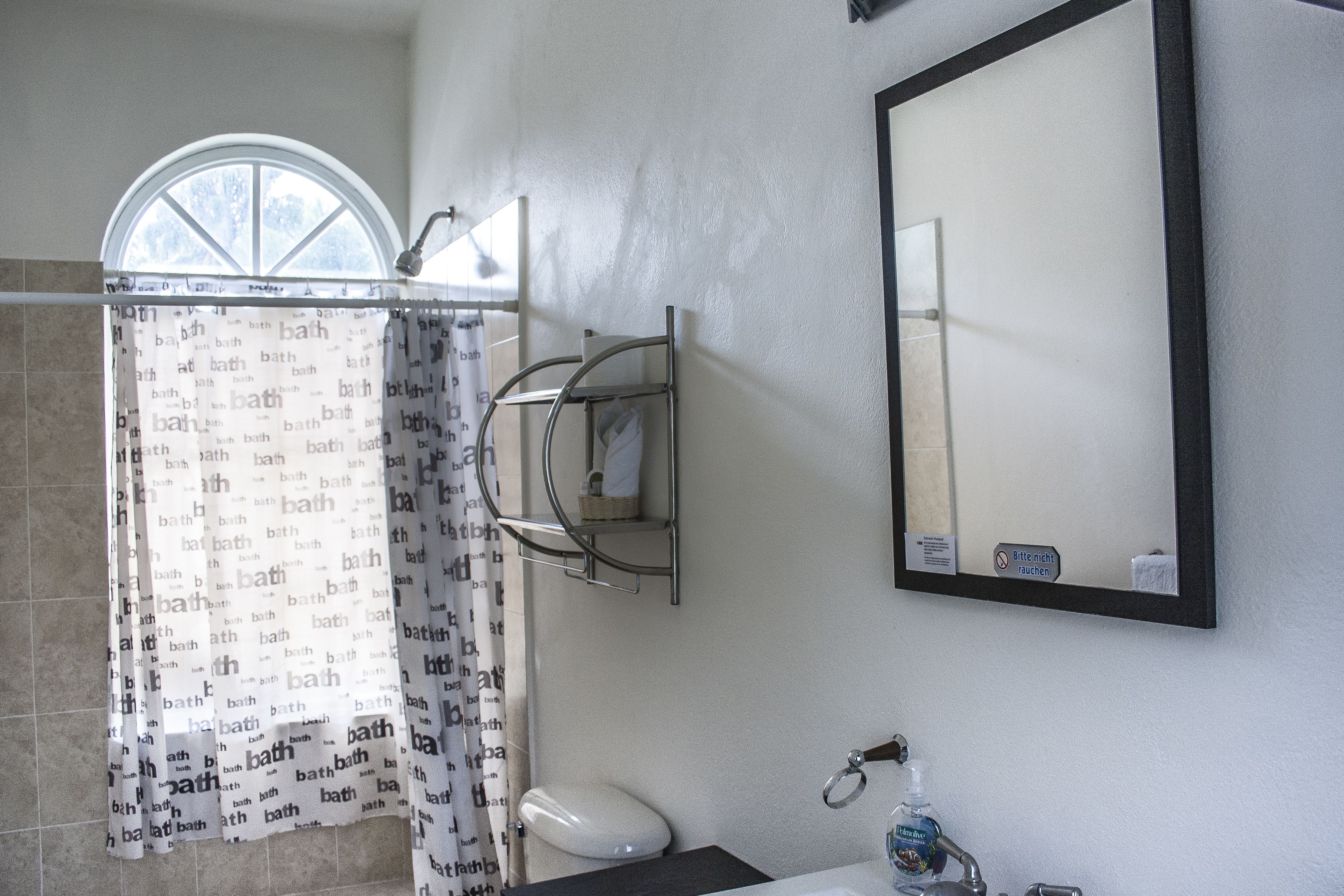 A bathroom with a shower curtain, a mirror, a towel rack, and a toilet.