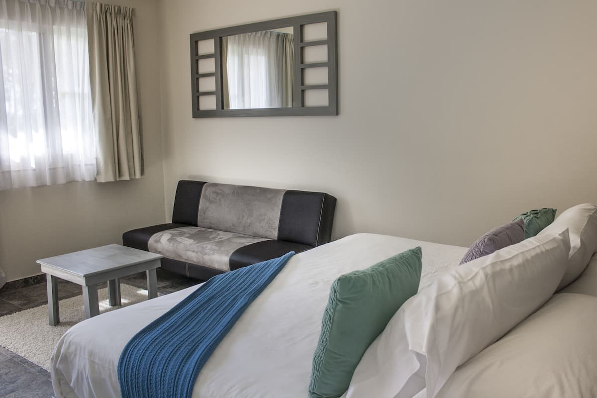 Habitación de hotel con cama, sofá, una mesita y un espejo en la pared.