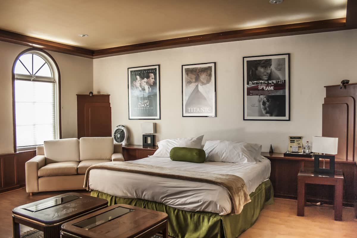 Habitación de hotel con una cama grande, un sofá, un escritorio y una ventana. Hay tres carteles en la pared.