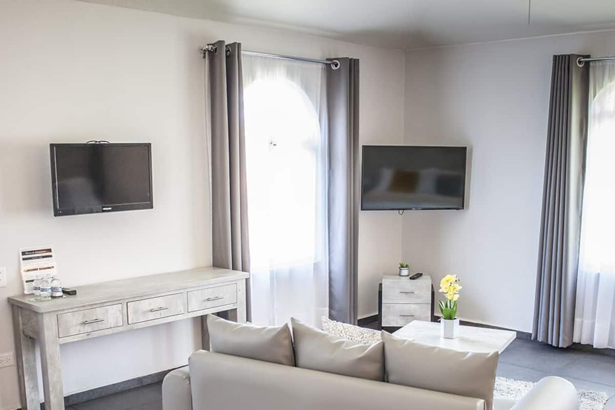 Una sala de estar moderna con un sofá, una mesa de centro, un televisor montado en la pared y una pequeña mesita con una planta.