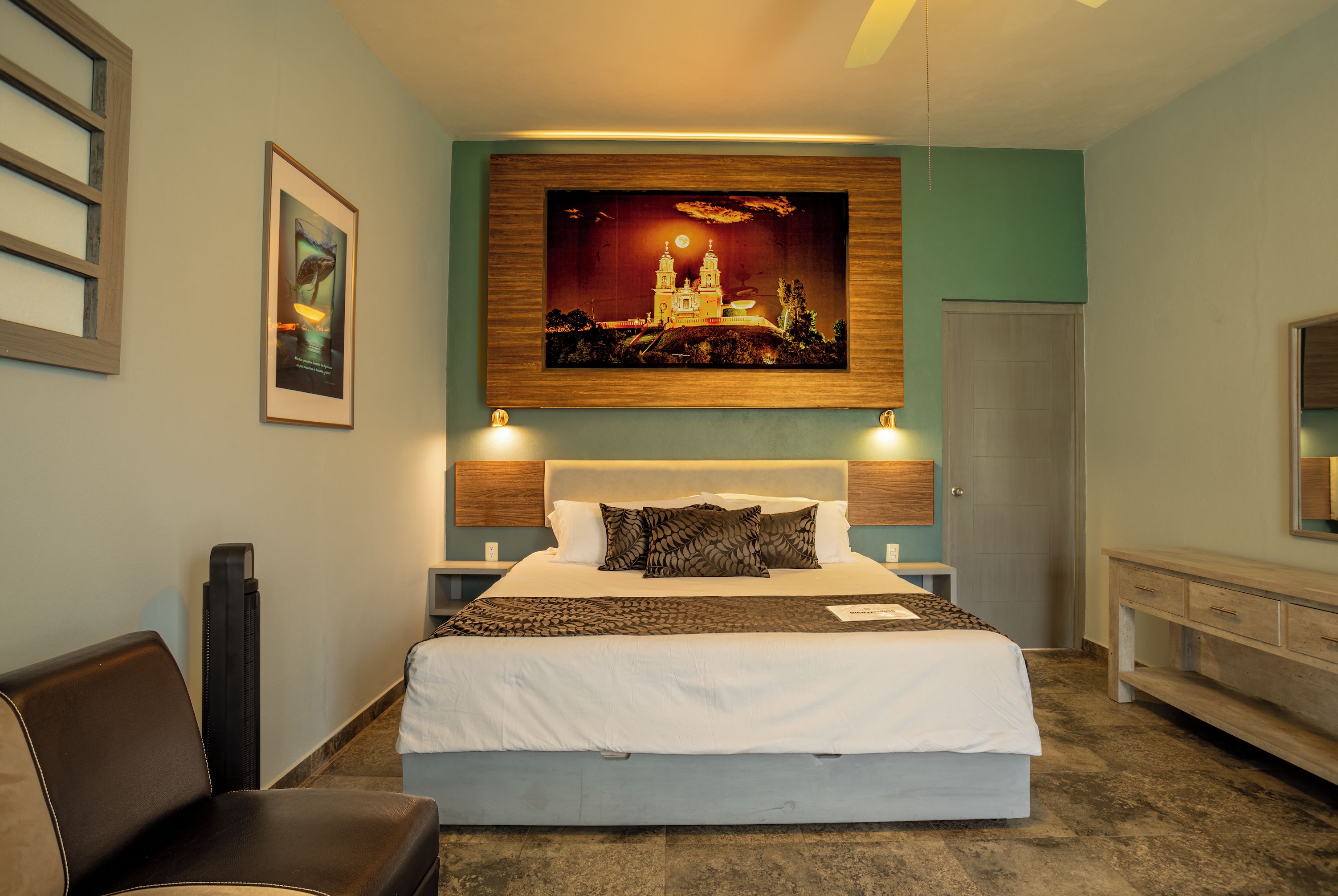 Una camera d'albergo con un letto grande, una testiera con pannello in legno, un comodino, una scrivania e una sedia.